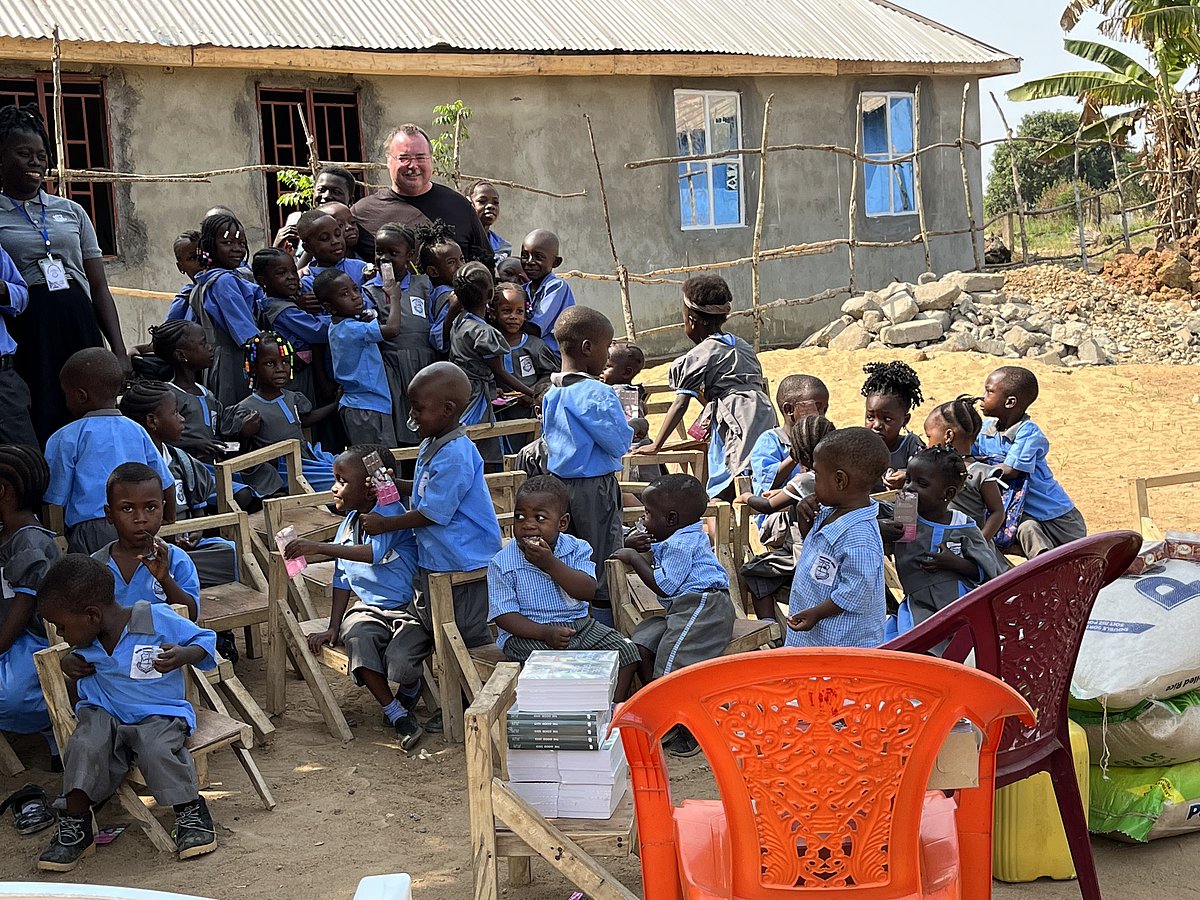 Ralf Döhring steht vor einer Schule in Sierra Leone und wird umringt von Schulkindern