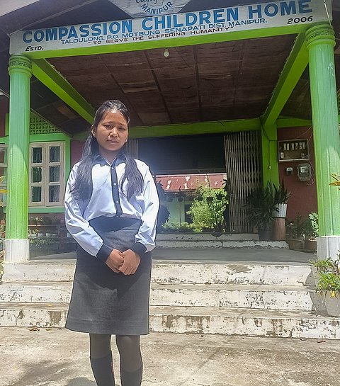 Ein Mädchen in Schuluniform steht vor einem Kinderheim in Indien