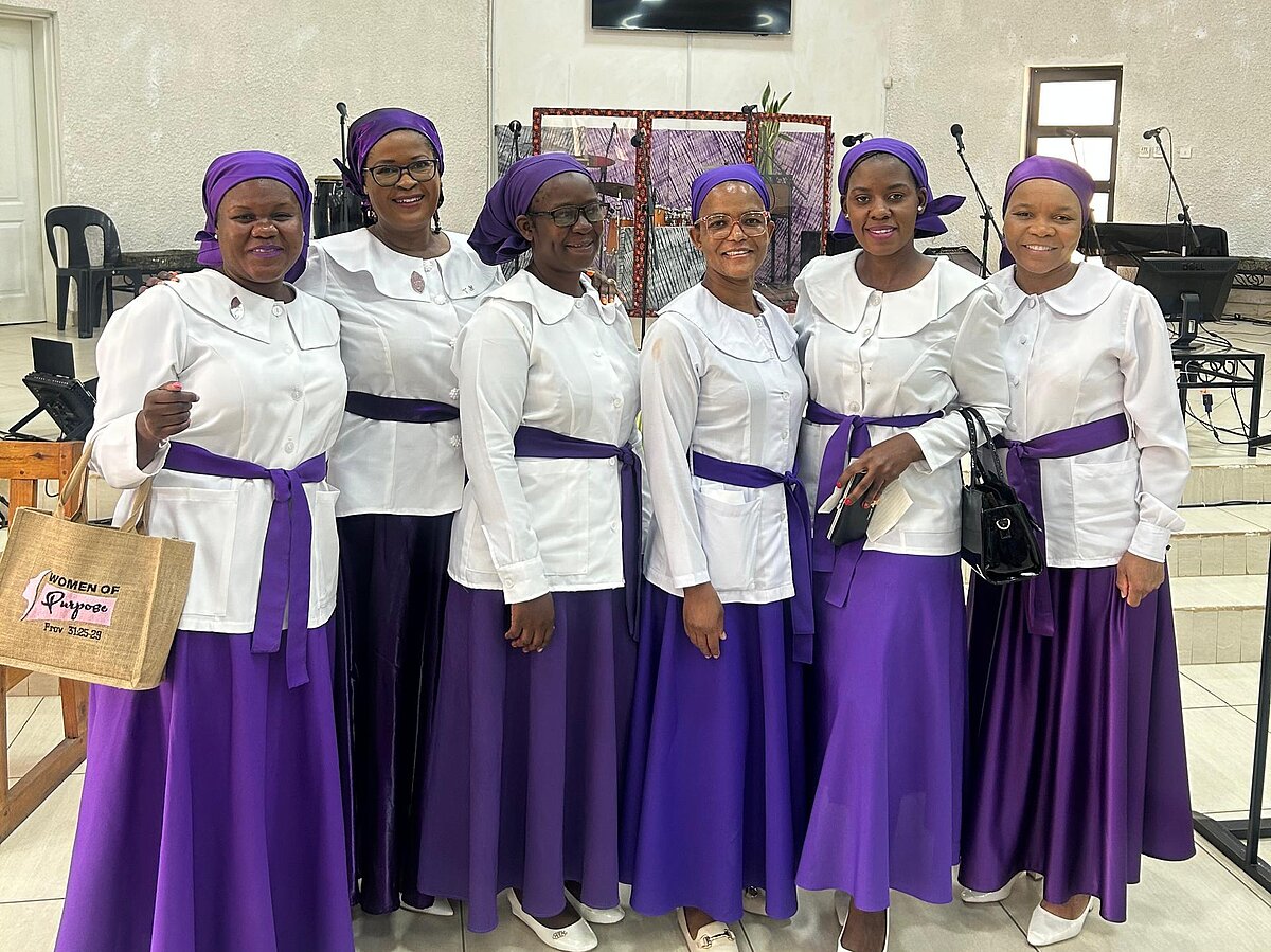 Eine Gruppe afrikanischer Frauen in weißen Blusen, violetten Röcken und violetten Kopftüchern bei einer Fortbildung.