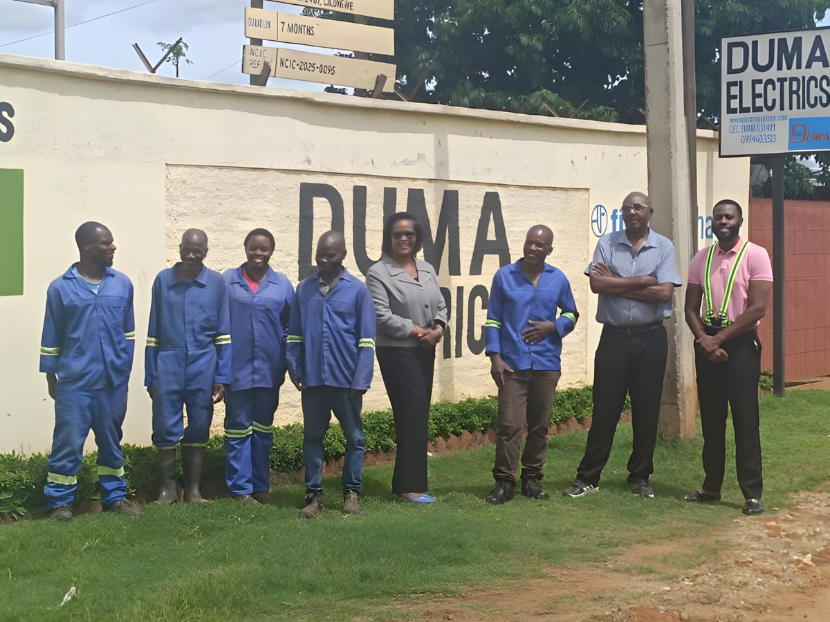 Vor der Außenmauer einer Elektronikfirma in Malawi steht die Belegschaft, zum Teil in blauen Overalls.