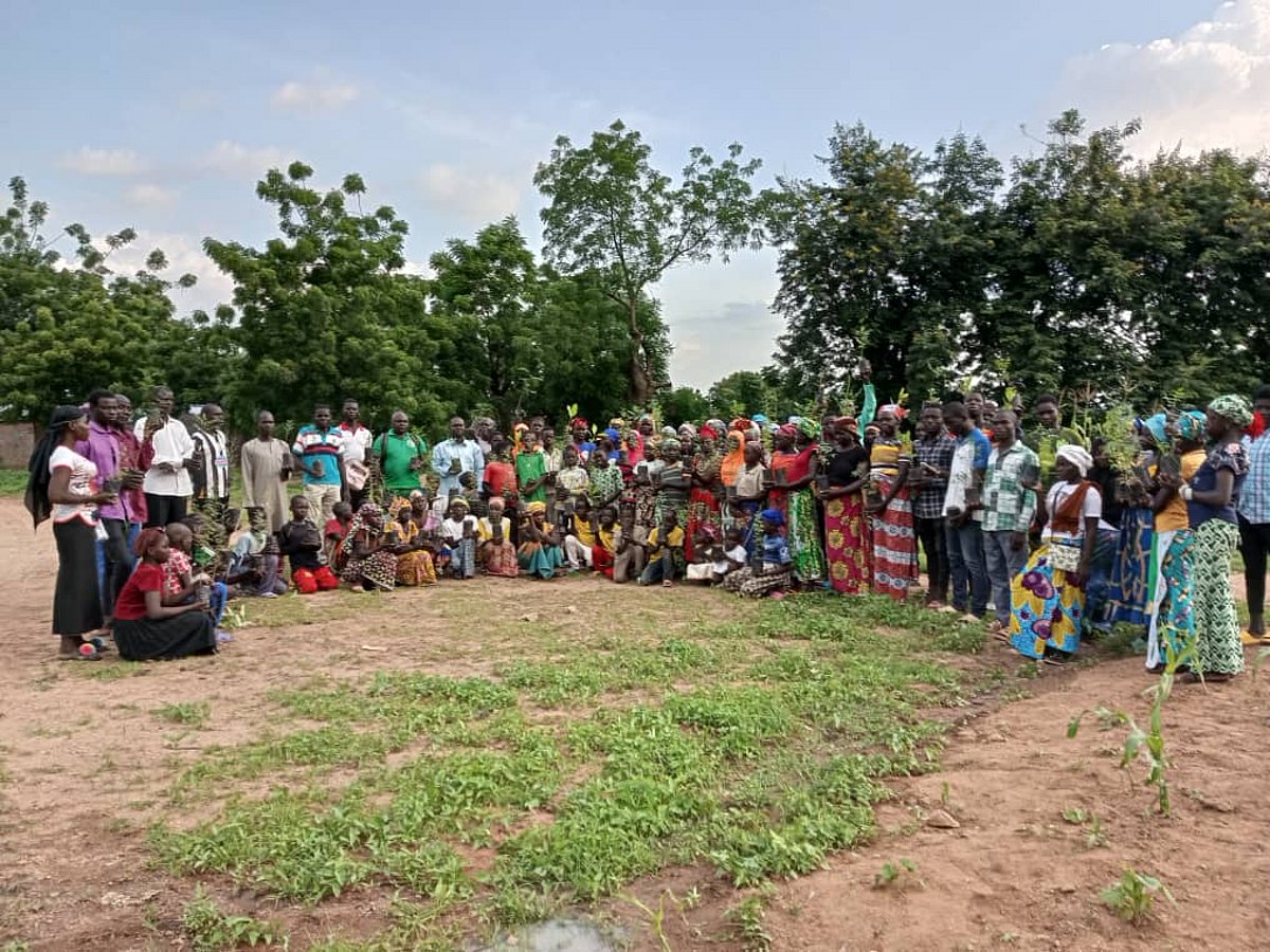Große Gruppe von Menschen steht in Kamerun auf einem Feld mit neu gepflanzten Setzlingen, im Hintergrund stehen Bäume