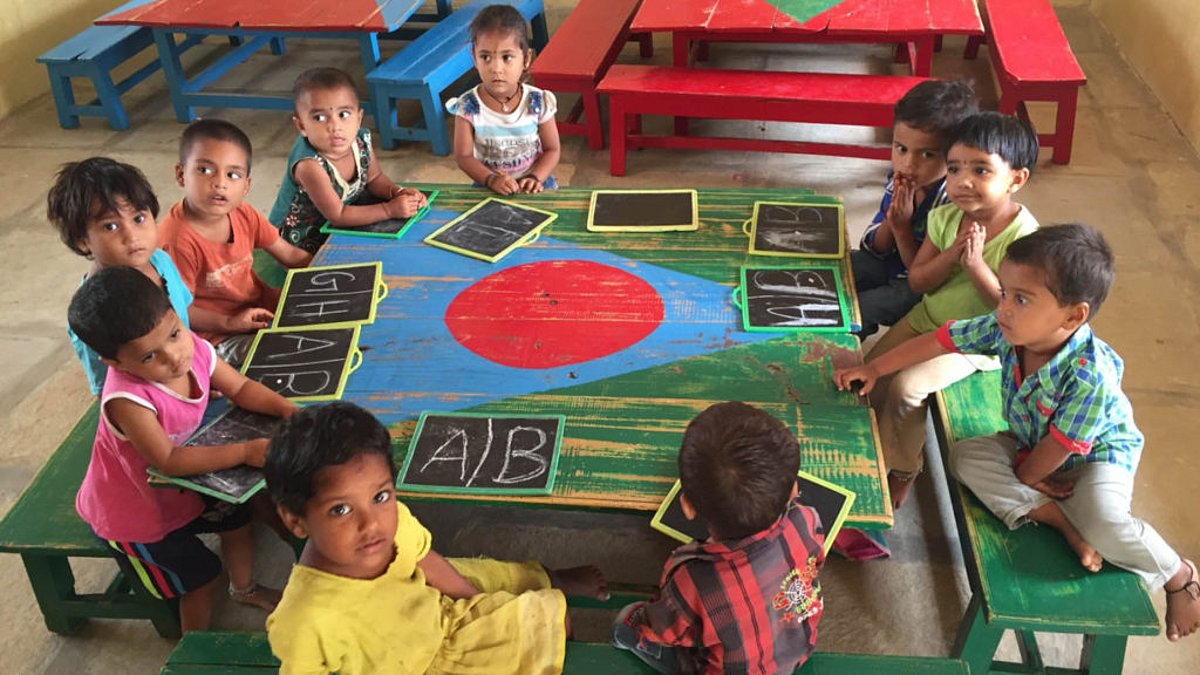 Eine Gruppe von Vorschulkindern sitzt gemeinsam um einen bunten Tisch und jedes Kind hat eine Tafel mit den Buchstaben A und B vor sich liegen