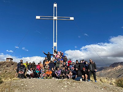 Große Gruppe von Menschen vor einem hohen weißen Kreuz auf einem Berg in Patagonien, Argentinien, bei klarem Himmel
