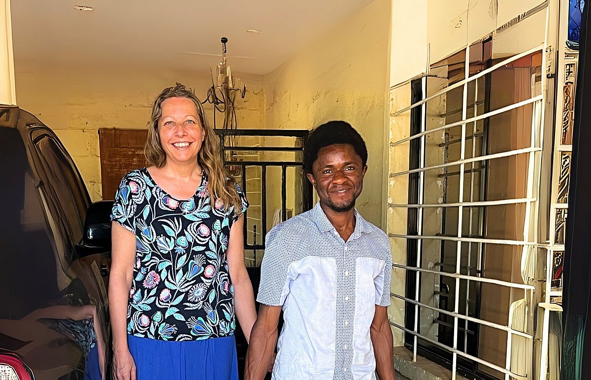 Missionarin Christina Döhring aus Deutschland steht gemeinsam mit Jeremia aus Sierra Leone vor einer gelben Wand