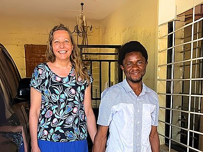 Missionarin Christina Döhring aus Deutschland steht gemeinsam mit Jeremia aus Sierra Leone vor einer gelben Wand