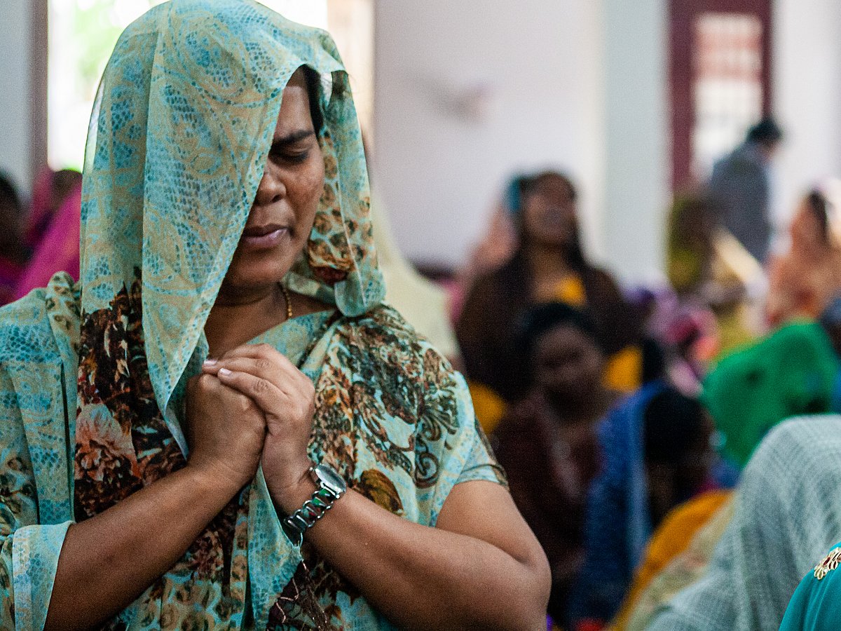 An Indian woman folds her hands and closes her eyes in prayer.