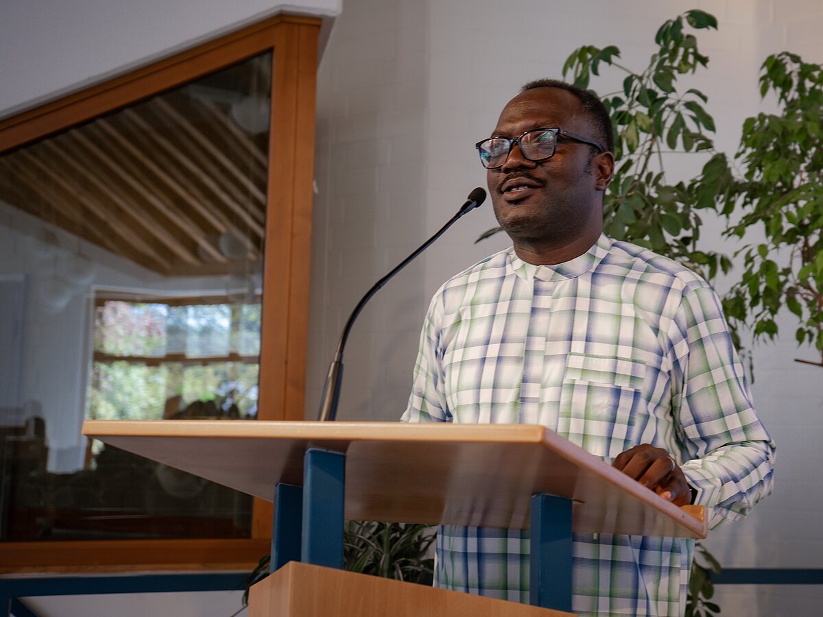 Ein nigerianische Mann steht vor einem Rednerpult.