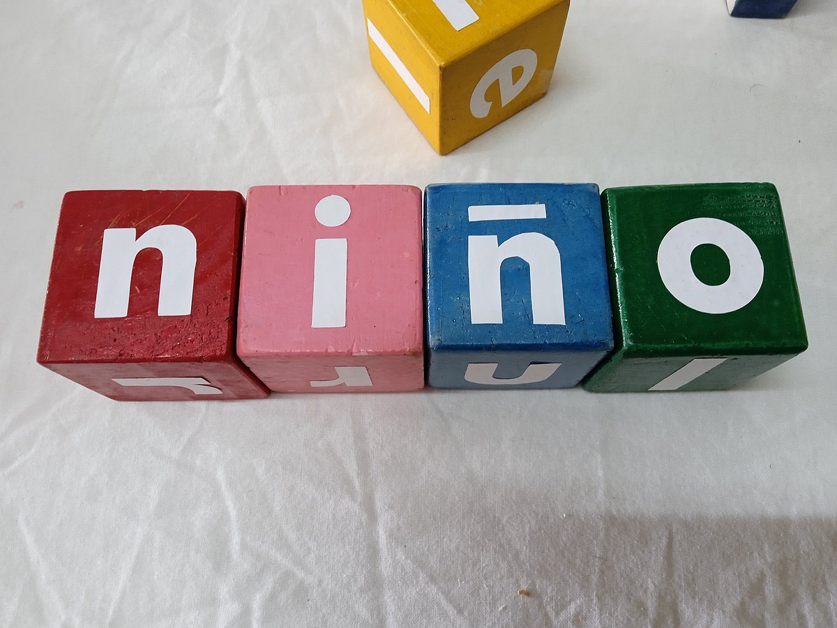 Vier bunte Holzklätze sind mit den Buchstaben für das spanische Wort für "Kind" beschriftet