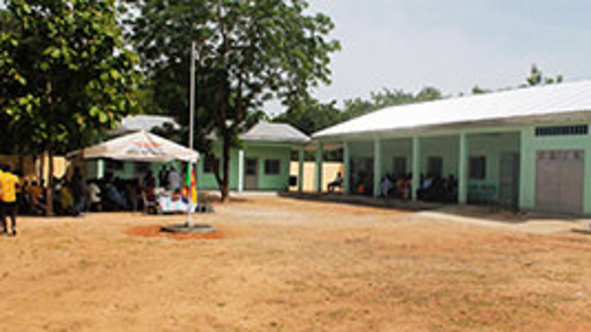 Innenhof eine Schule in Afrika mit grün gestrichenen Gebäuden, Menschen unter Sonnenschirmen und Bäumen